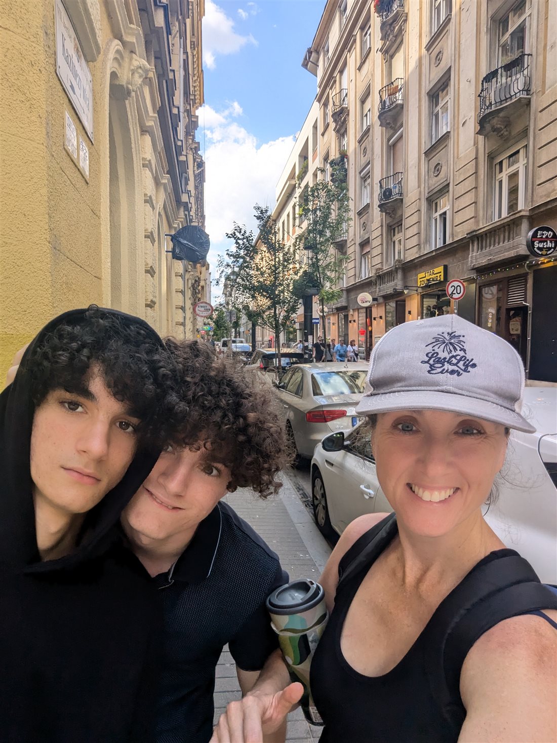 Jillian in a Last Life Ever cap taking a selfie with her two sons on a street in Budapest