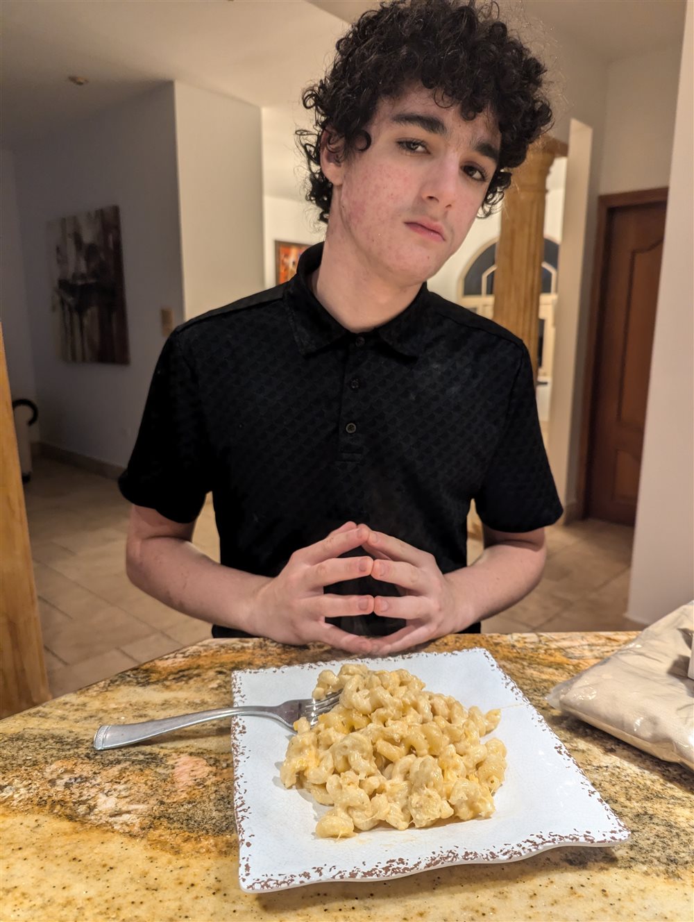 Tom, 15, at the kitchen counter with a plate of mac and cheese, giving a deadpan look