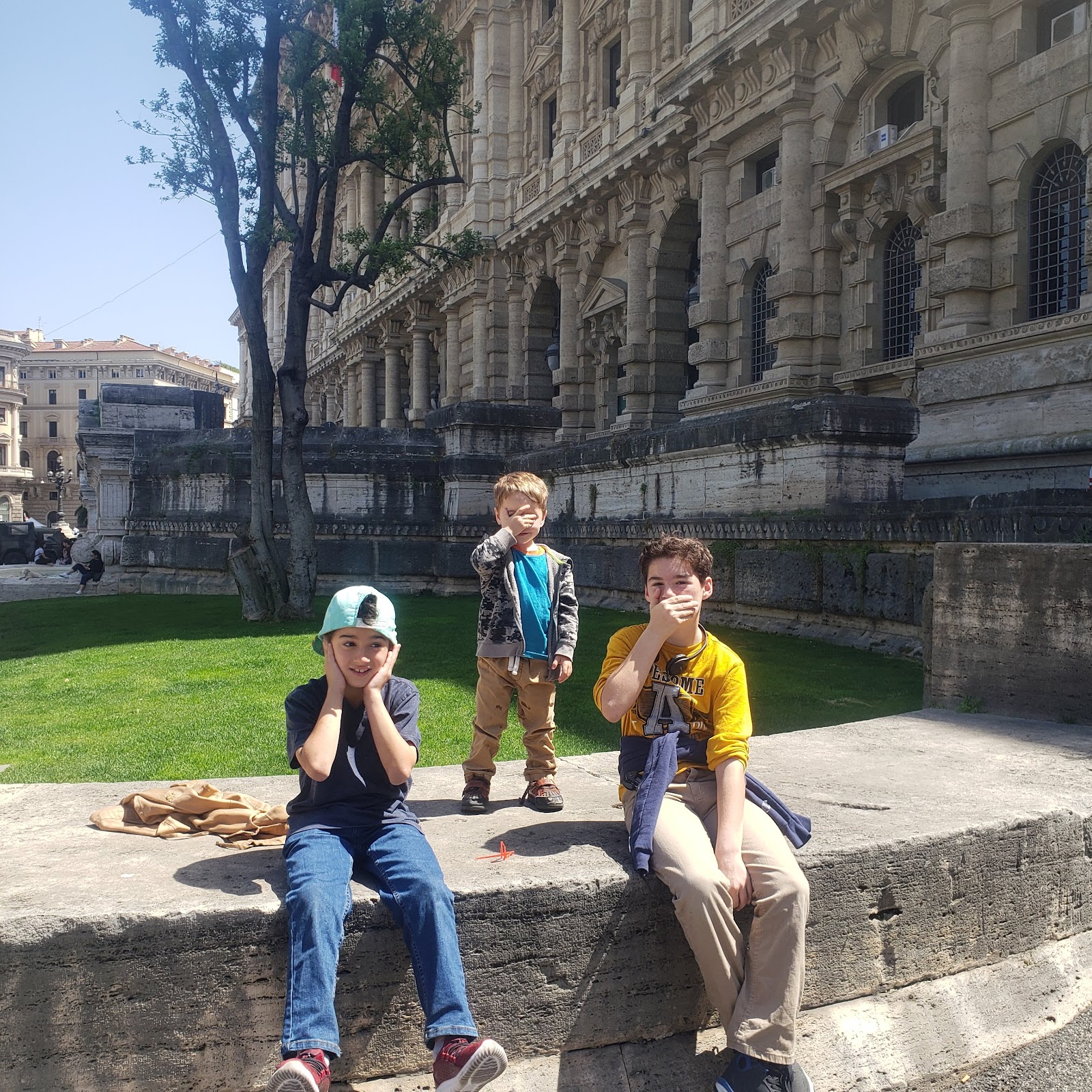 The three kids being themselves on a stone wall in Rome